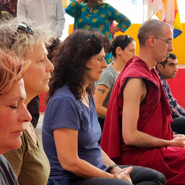 Groupe en méditation bouddhiste avec moine en robe rouge, drapeaux tibétains en arrière-plan