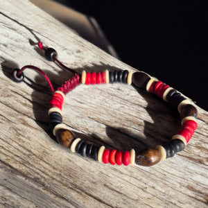 Bracelet bouddhiste tibétain en perles rouges, noires et bois, posé sur bois brut