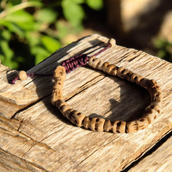 Bracelet bouddhiste en perles sculptées, symbole de méditation et philosophie tibétaine, posé sur bois