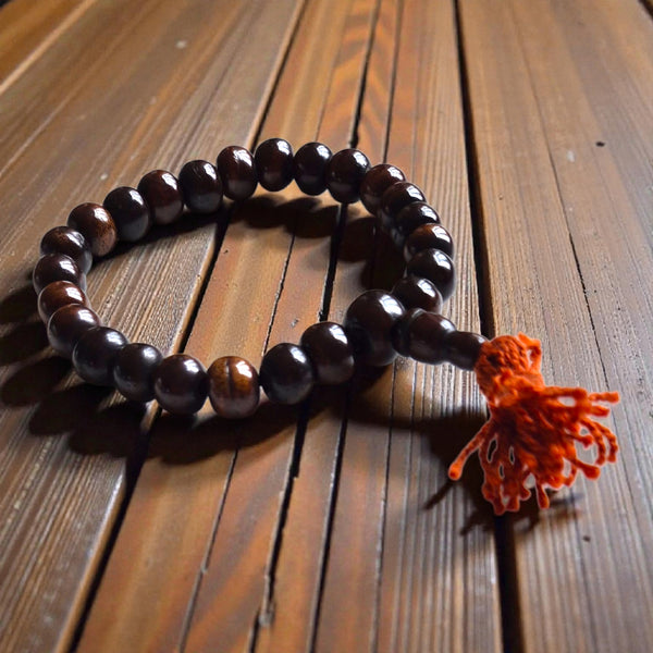 Chapelet bouddhiste en bois foncé avec pompon orange, posé sur bois, pour méditation et philosophie tibétaine