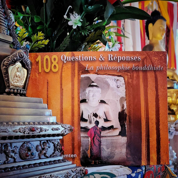 Livre 108 Questions & Réponses sur la philosophie bouddhiste, entouré d'objets tibétains et de fleurs