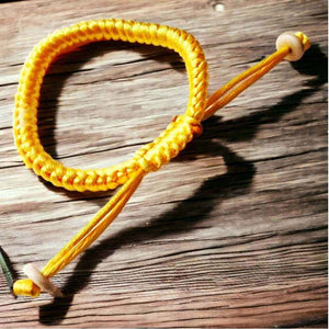 Bracelet tibétain tressé jaune, symbole de sagesse bouddhiste, posé sur bois