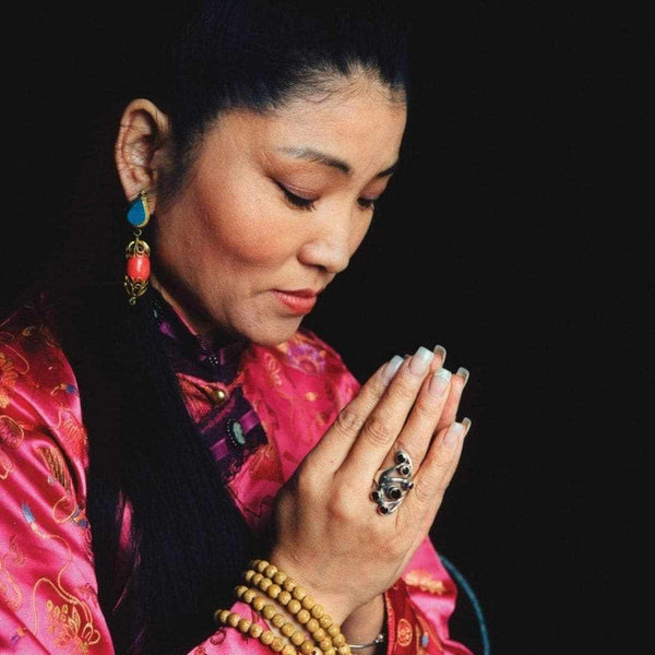 Femme en tenue tibétaine priant avec perles de méditation, bijoux traditionnels et anneau bouddhiste