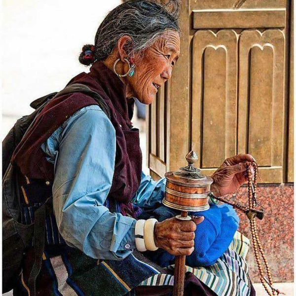 Femme tibétaine âgée priant avec moulin à prières et chapelet, culture bouddhiste himalayenne