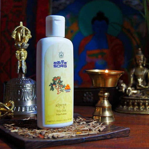 Lotion Tripa Sorig, produit naturel de médecine tibétaine, entourée d'objets bouddhistes et d'herbes séchées.