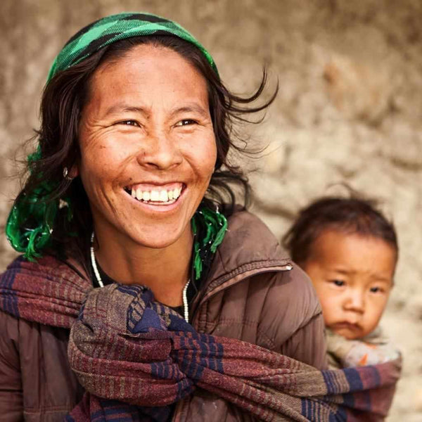Femme tibétaine souriante avec bébé, écharpe traditionnelle, culture himalayenne