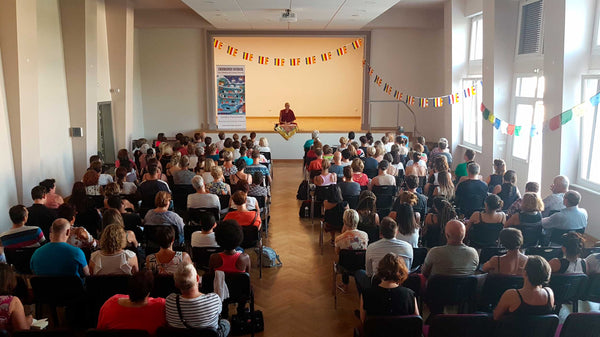 Conférence sur la méditation bouddhiste tibétaine avec un maître devant un public, drapeaux tibétains