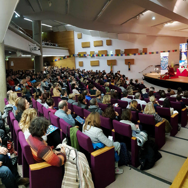 Conférence de méditation bouddhiste avec public attentif dans une salle décorée de drapeaux tibétains