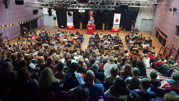 Conférence de méditation bouddhiste avec Lama Samten devant un public nombreux, drapeaux tibétains et décor spirituel