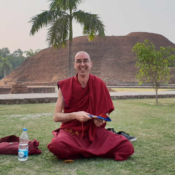 Moine bouddhiste en robe rouge méditant sur l'herbe près d'une stupa, avec palmier et culture tibétaine