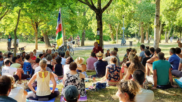 Groupe en méditation bouddhiste en plein air sous les arbres, avec drapeau tibétain et enseignement