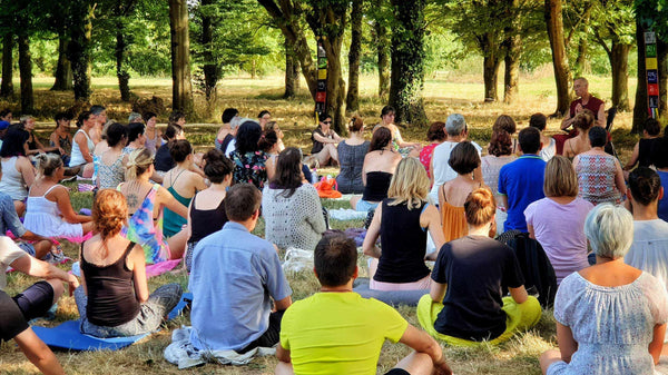Groupe en méditation bouddhiste en plein air, enseignement en forêt avec drapeaux tibétains