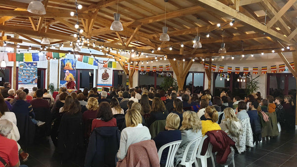 Conférence de méditation bouddhiste avec public dans salle en bois, drapeaux tibétains et enseignement spirituel