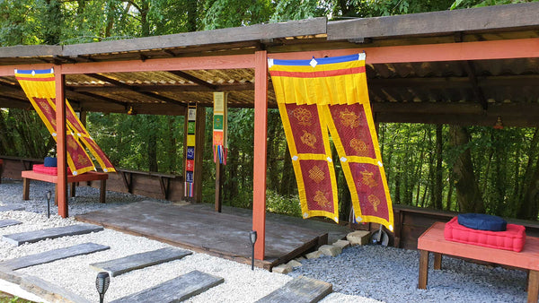 Espace de méditation en plein air avec drapeaux tibétains, coussins et pergola bois, idéal pour la pratique bouddhiste.