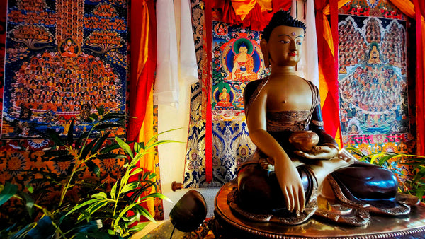 Statue de Bouddha assis avec thangkas tibétains et offrandes, symboles de la philosophie bouddhiste