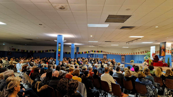 Conférence sur la méditation avec un moine bouddhiste devant un public attentif, drapeaux tibétains en arrière-plan