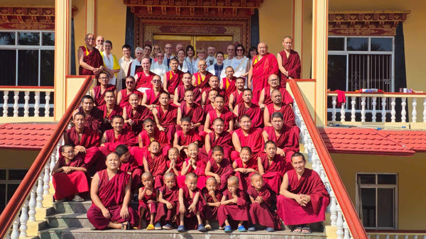 Groupe de moines bouddhistes tibétains en robes rouges sur les marches d'un temple, avec visiteurs