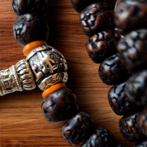 Perles de prière bouddhistes tibétaines en bois sculpté et métal orné, posées sur bois