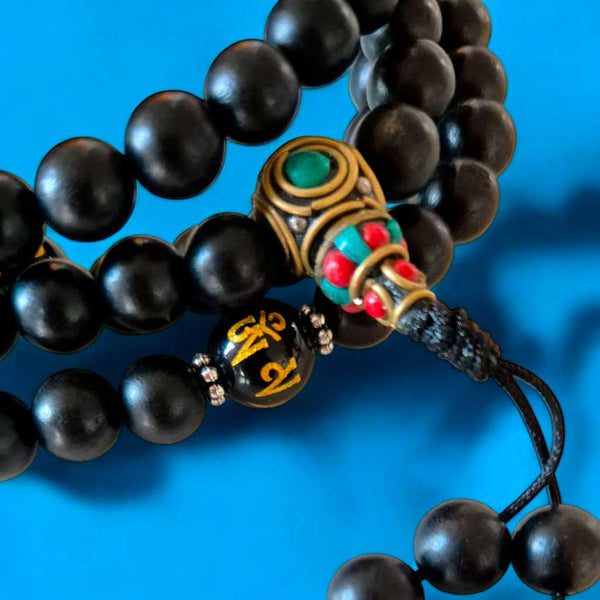 Chapelet bouddhiste noir avec perles décoratives et symboles tibétains sur fond bleu