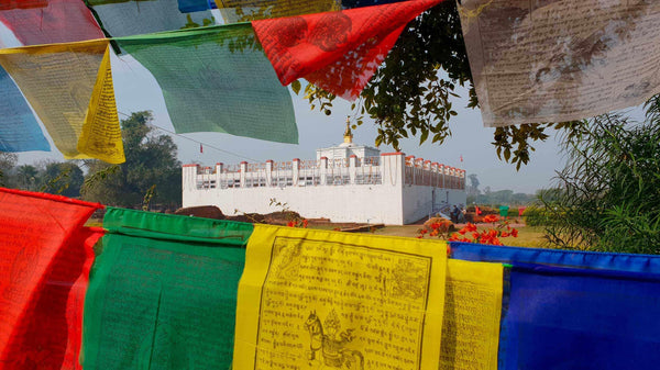 Drapeaux de prière bouddhistes colorés devant un temple blanc, symboles de la culture tibétaine et de la méditation.