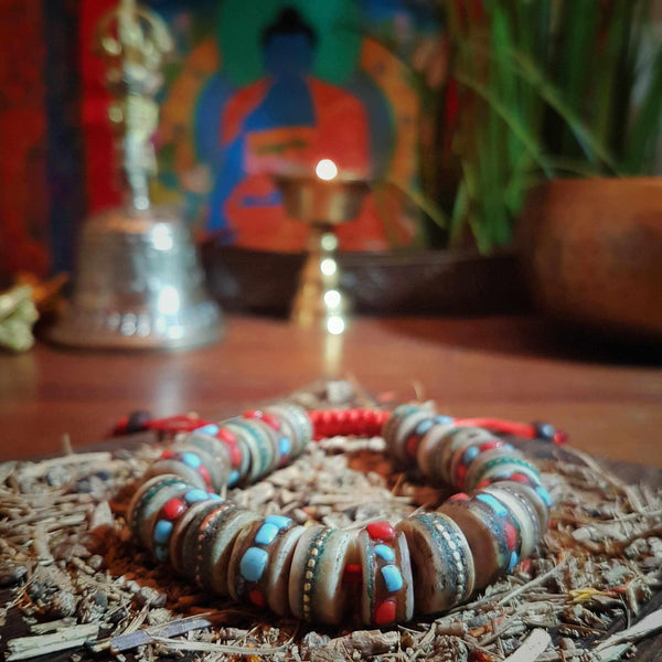 Bracelet tibétain en perles colorées avec turquoise et corail, devant une statue de Bouddha et une lampe à huile.