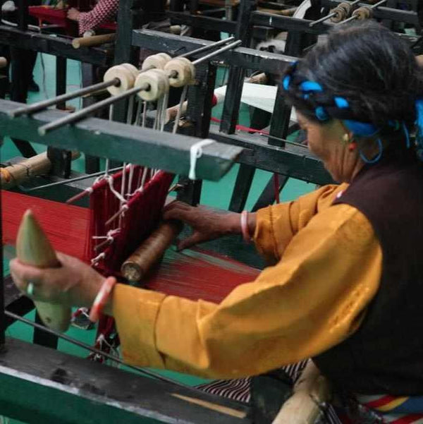 Artisan tibétain tissant un tissu rouge sur métier à tisser traditionnel, culture himalayenne
