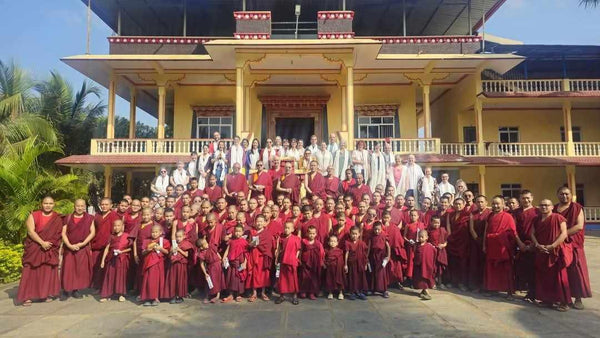Groupe de moines bouddhistes tibétains en robes rouges devant un centre spirituel, avec visiteurs et enseignants