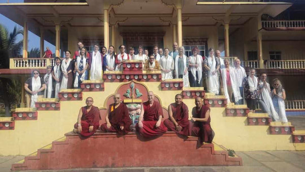 Groupe de moines bouddhistes et visiteurs en tenue traditionnelle devant un temple tibétain