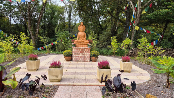 Statue de Bouddha en méditation dans jardin zen avec drapeaux tibétains et plantes apaisantes