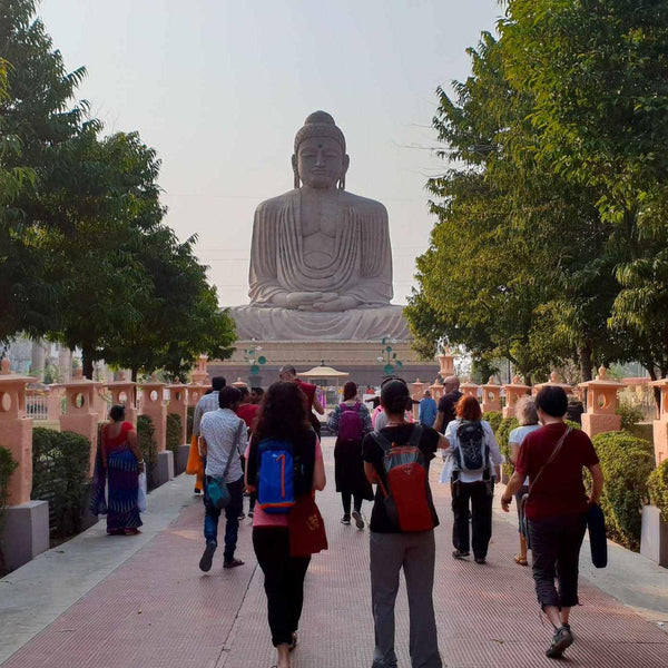 Statue géante de Bouddha assis, pèlerins marchant sur allée bordée d'arbres, symbole de méditation et sérénité