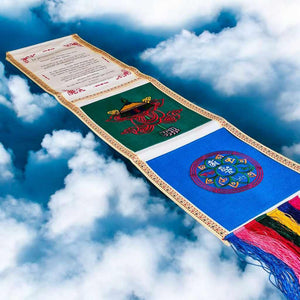 Drapeau de prière tibétain brodé avec symboles bouddhistes et franges colorées sur fond de nuages
