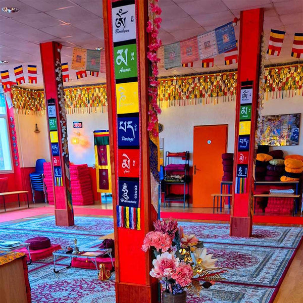 Salle de méditation bouddhiste avec drapeaux tibétains, tapis colorés et colonnes décorées de symboles spirituels