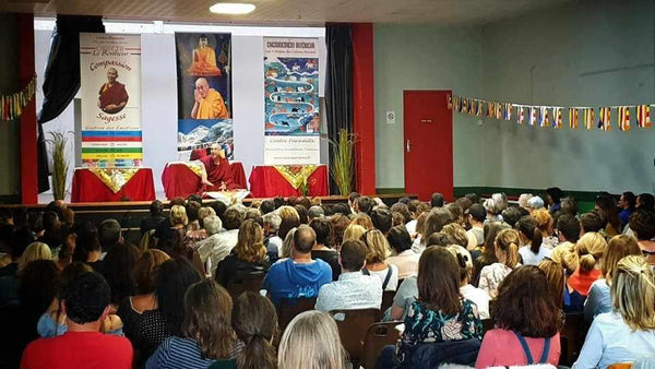 Conférence de méditation bouddhiste avec Lama Samten devant un public, drapeaux tibétains et affiches philosophiques