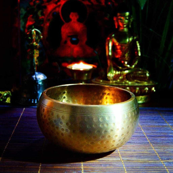 Bol tibétain en cuivre martelé pour méditation, avec statues bouddhistes en arrière-plan