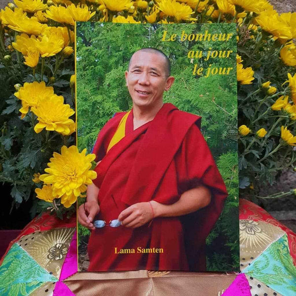 Livre 'Le bonheur au jour le jour' par Lama Samten, entouré de fleurs jaunes, vêtements bouddhistes rouges
