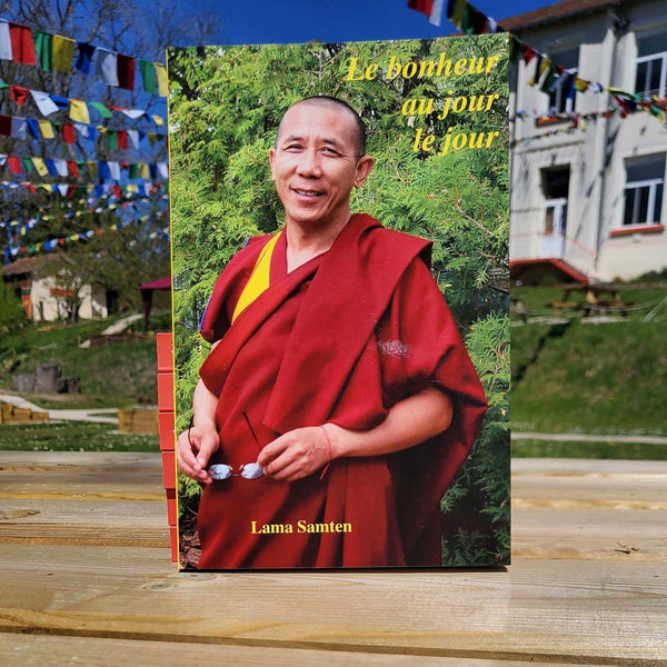Livre 'Le bonheur au jour le jour' par Lama Samten, robe rouge, drapeaux tibétains en arrière-plan