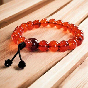 Bracelet de méditation en perles d'ambre rouge avec nœud noir, posé sur bois clair