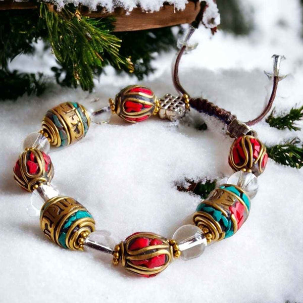 Bracelet bouddhiste tibétain en perles colorées et métal doré, posé sur la neige avec branches de sapin