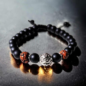 Bracelet bouddhiste avec perles noires, motifs tibétains et pendentif métallique, symbole de méditation et sagesse.