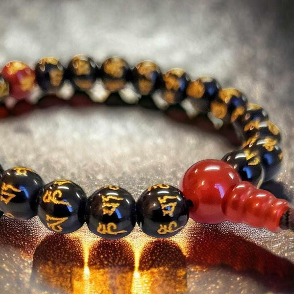 Bracelet bouddhiste avec perles noires gravées de mantras tibétains et perle rouge en agate