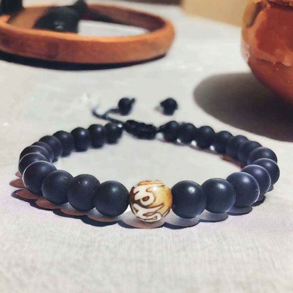 Bracelet bouddhiste en perles noires avec perle centrale gravée, symbole de méditation et philosophie tibétaine