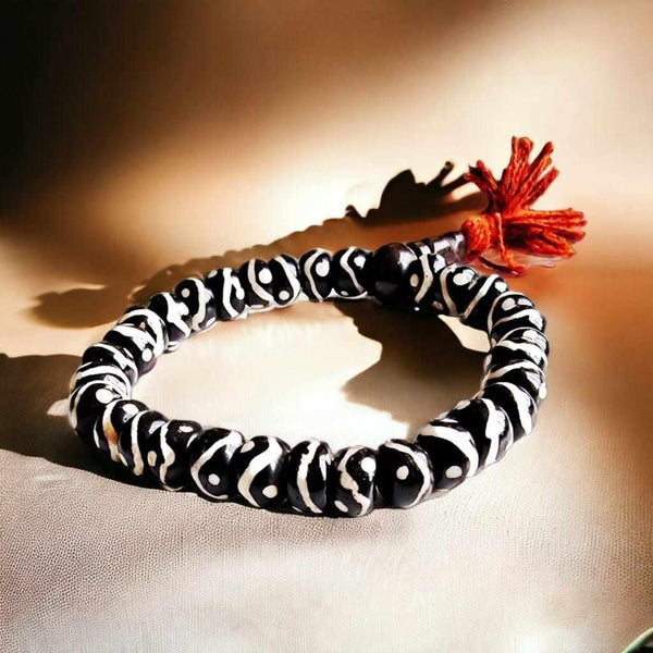 Bracelet bouddhiste en perles noires et blanches avec pompon rouge, symbole de la philosophie tibétaine
