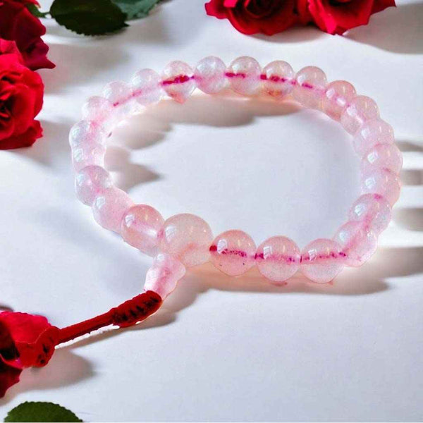 Bracelet en perles roses translucides avec nœud rouge, entouré de roses rouges