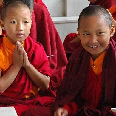 Jeunes moines bouddhistes tibétains en robes rouges priant et souriant, culture spirituelle de l'Himalaya