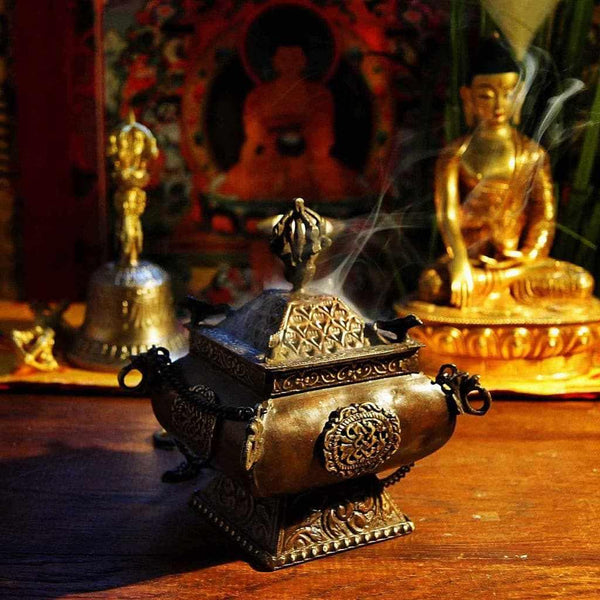 Encensoir bouddhiste tibétain en métal orné, fumée s'élevant, statue de Bouddha dorée en arrière-plan
