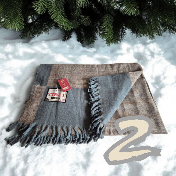 Châle tibétain en laine à franges, posé sur la neige sous un sapin, avec étiquette 'TIBET SHAWL'