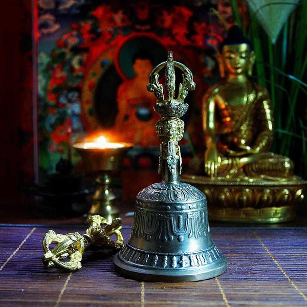 Cloche et vajra bouddhiques tibétains sur tapis de méditation, statue de Bouddha en arrière-plan