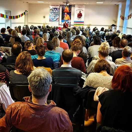 Conférence sur la méditation bouddhiste avec public attentif, décor tibétain et drapeaux colorés