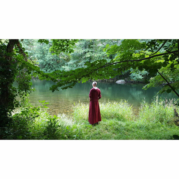 Moine bouddhiste en robe rouge méditant près d'une rivière en forêt, sérénité et philosophie tibétaine