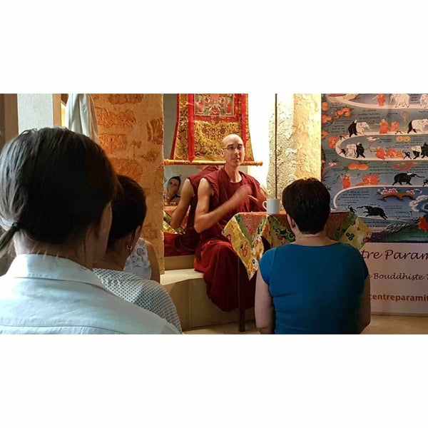 Lama en robe rouge enseignant la méditation bouddhiste devant un public, avec thangka tibétain en arrière-plan